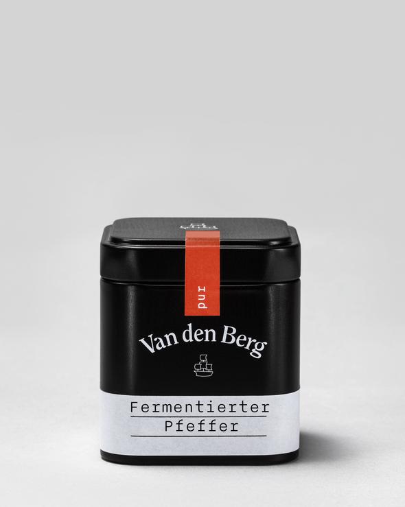 Eine schwarze rechteckige Dose mit der Aufschrift „Van den Berg“ und „pur“ auf einem roten Streifen steht vor einem schlichten hellgrauen Hintergrund. Das Etikett mit der Aufschrift „Fermentierter Pfeffer“ auf Deutsch deutet auf Aromen hin, die sich perfekt zum Verfeinern traditioneller Gerichte wie Schwäbischer Kartoffelsalat eignen.