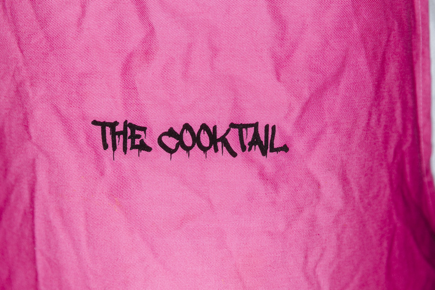 Ein rosa Stoffhintergrund mit den Worten „THE COOKTAIL“, die in der Mitte in schwarzer Graffiti-Buchstabe aufgedruckt sind und eine kräftige und dynamische Energie hervorrufen, die an die Kunst des Kung Fu erinnert.